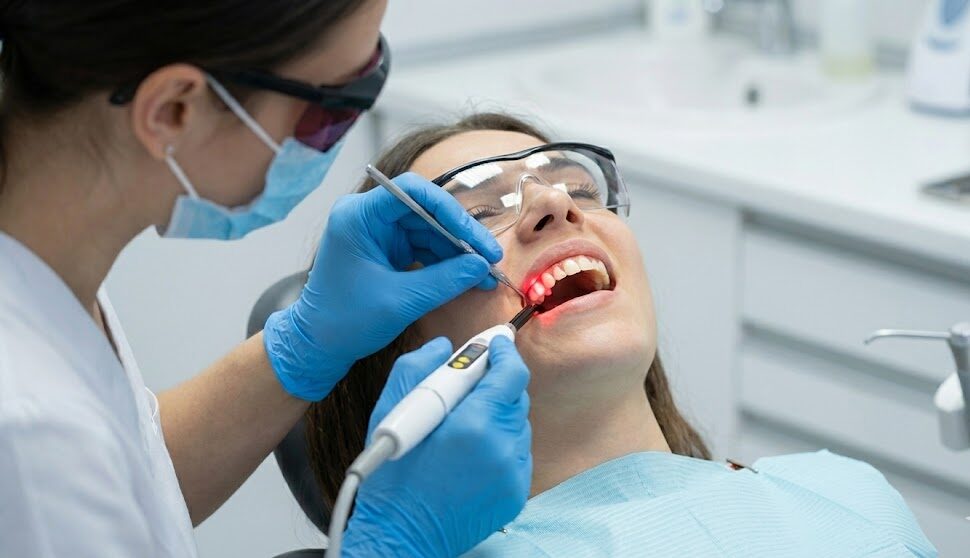 A dentist uses a laser device on a patient's gums during a laser gum therapy session.