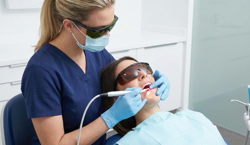 A dentist using a dental laser handpiece to treat a patient's gum tissue in a modern dental clinic.