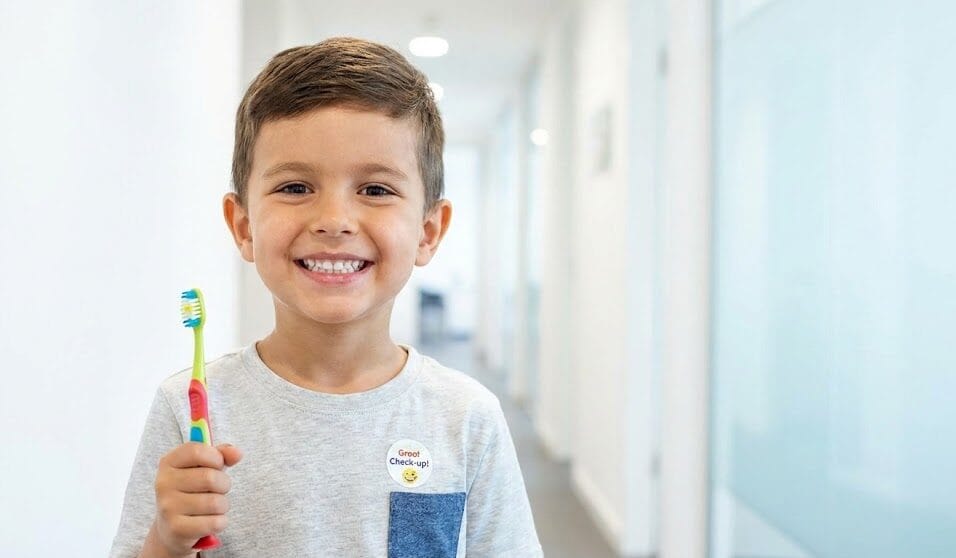 A happy young boy smiling proudly and holding a toothbrush after a positive dental check-up.